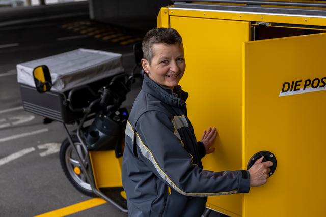 An employee opens a side compartment of a yellow delivery vehicle next to an electric delivery scooter. An employee opens a side compartment of a yellow delivery vehicle next to an electric delivery scooter.