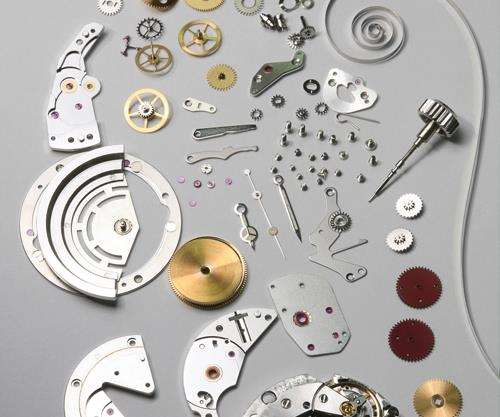 Photo macro de nombreux composants d’un mécanisme de montre étalés sur un établi – engrenages, ressorts et pièces mécaniques fines.