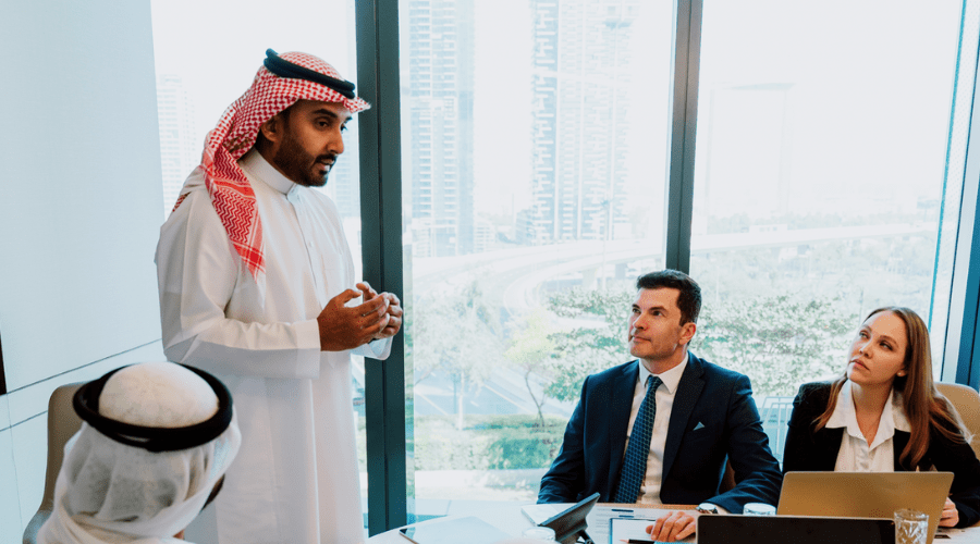 Corporate business event with emirati and western business people. middle eastern saudi businessman standing and actively explaining ideas to colleagues 