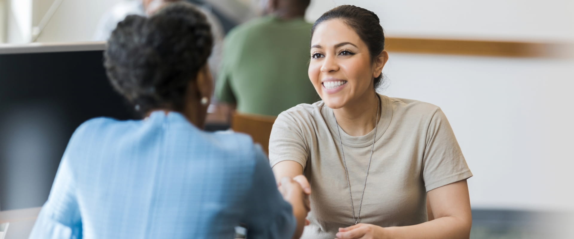 A smiling veteran in partial uniform shakes hands with a hiring manager across the desk. A smiling veteran in partial uniform shakes hands with a hiring manager across the desk.