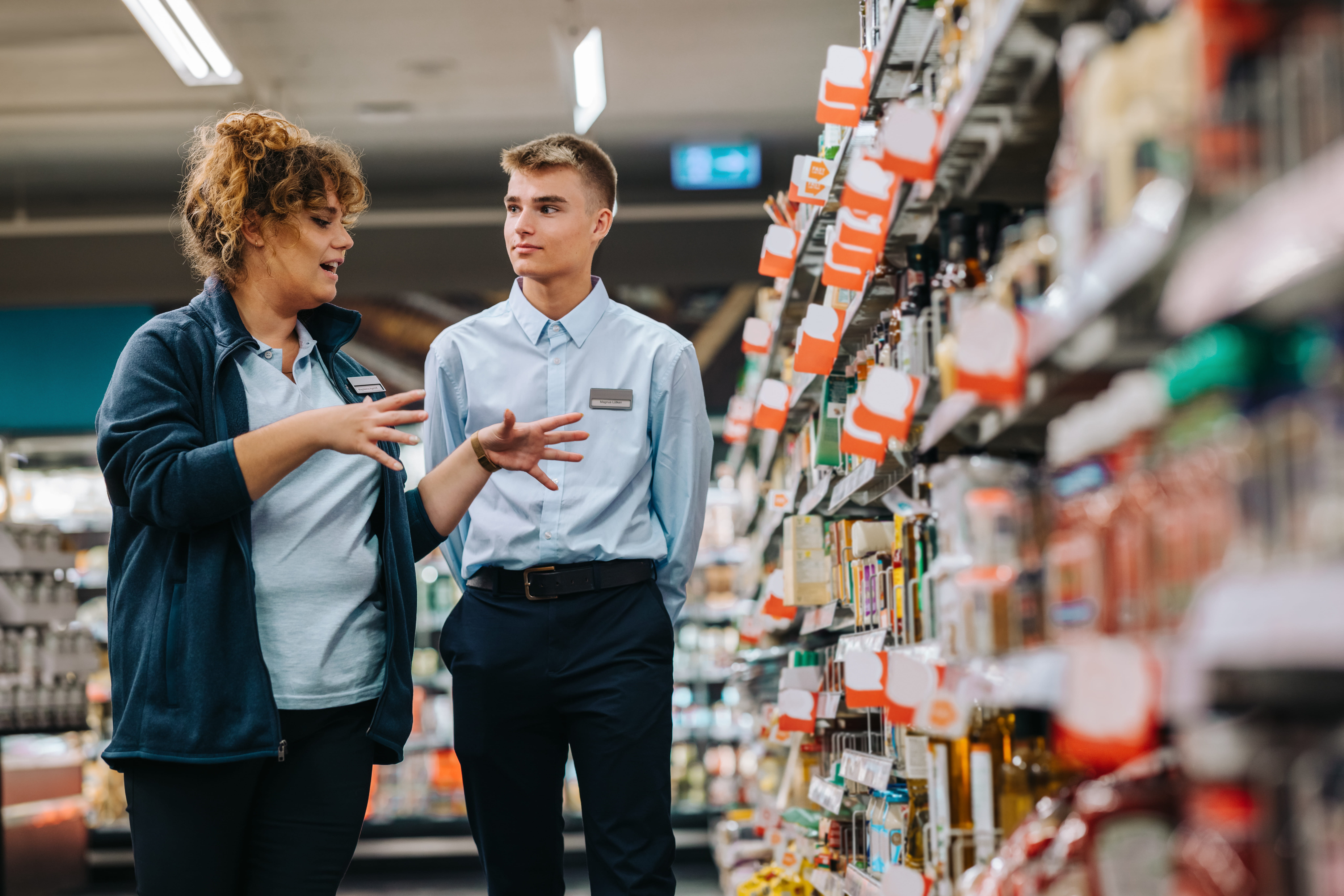 Des marchandiseurs en commerce de détail parlent de rabais et de livraisons dans une allée remplie de produits bien rangés. Des marchandiseurs en commerce de détail parlent de rabais et de livraisons dans une allée remplie de produits bien rangés.