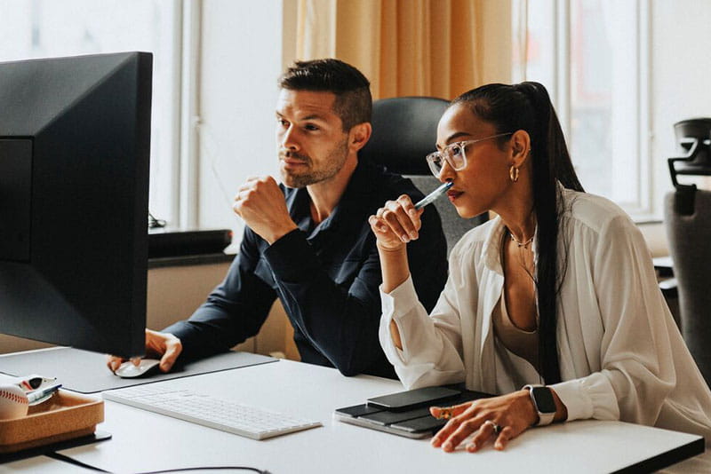 Two colleagues reviewing information on a computer in an office Two colleagues reviewing information on a computer in an office