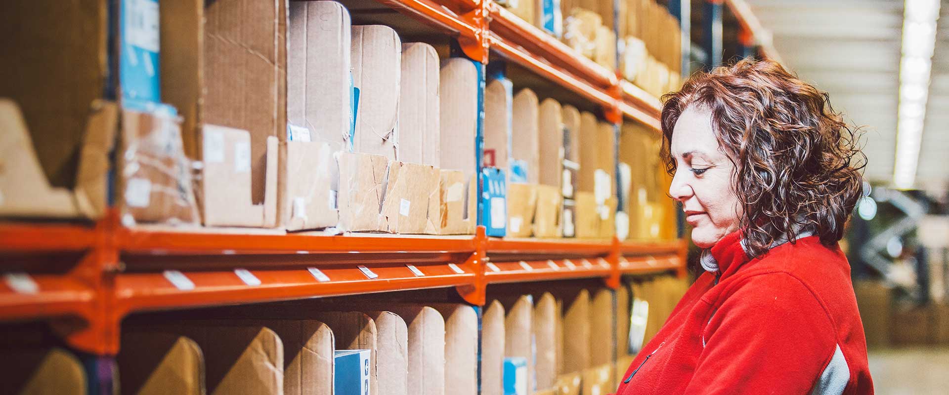 Employé d'entrepôt en chemise rouge vérifiant l'inventaire sur des étagères de stockage