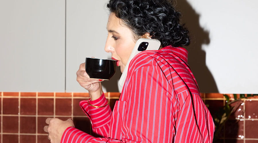 Kvinna dricker kaffe och talar i telefon i kök