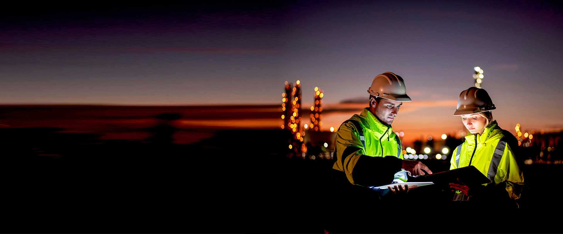 Energy workers reviewing plans at industrial site at sunset