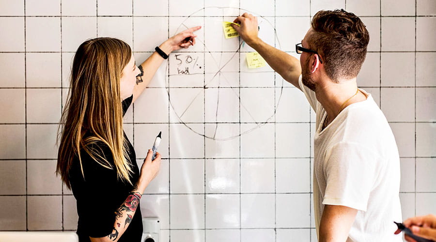 Two colleagues writing on board during brainstorming