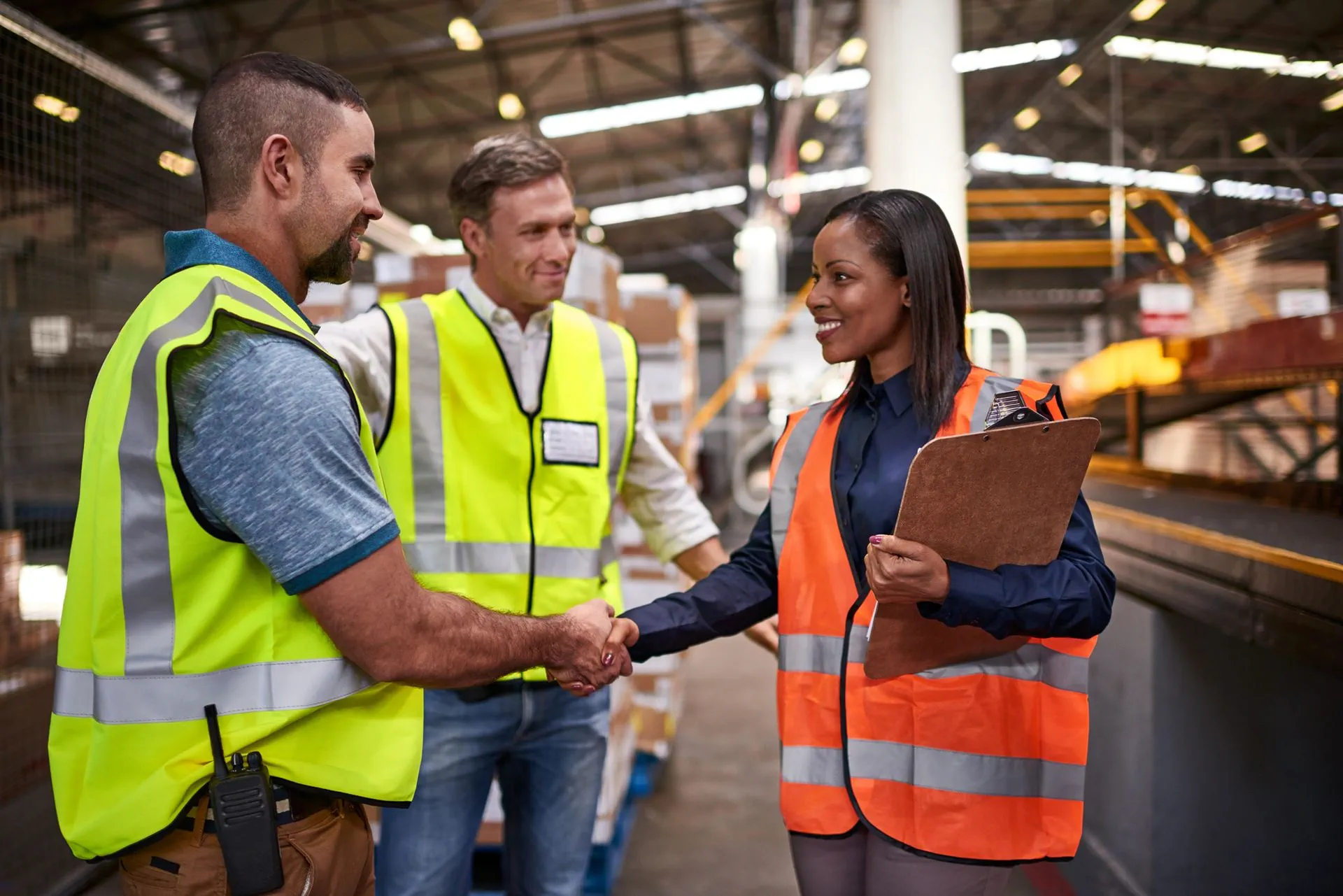 Three workers in a warehouse wearing safety vests
