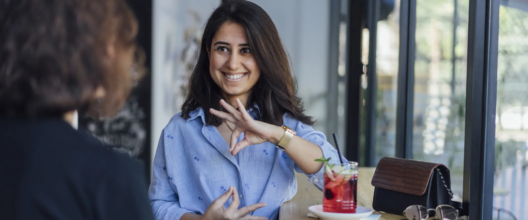 Two people sit at a coffee shop speaking in sign language.