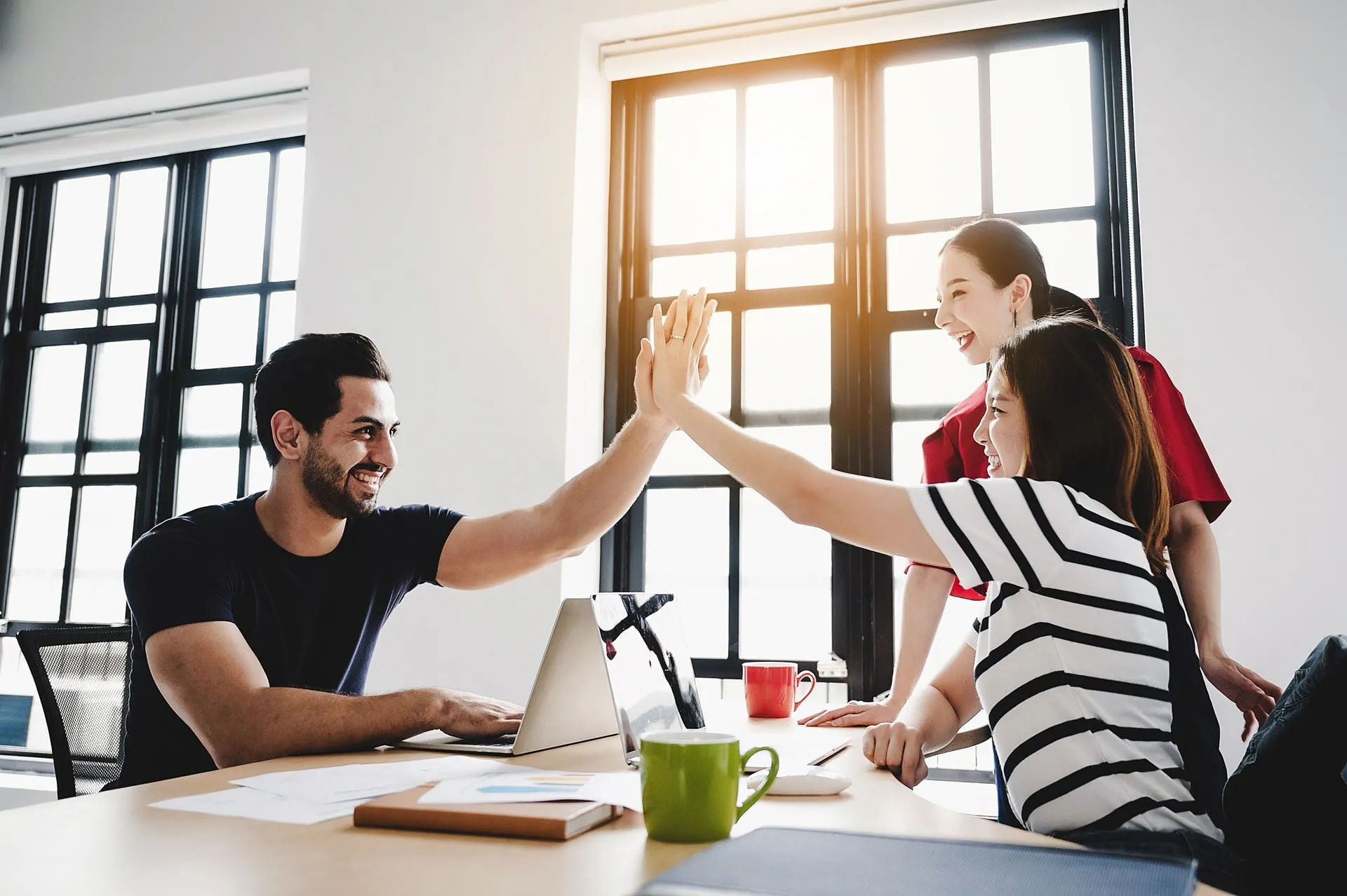Team members giving a high five in a bright and modern office, celebrating success and teamwork.
