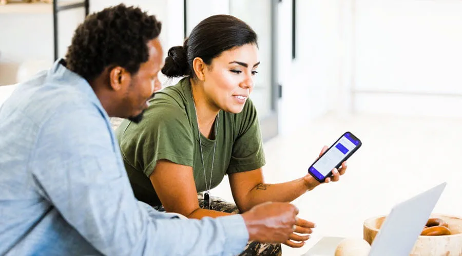 Two people reviewing information on a smartphone and laptop