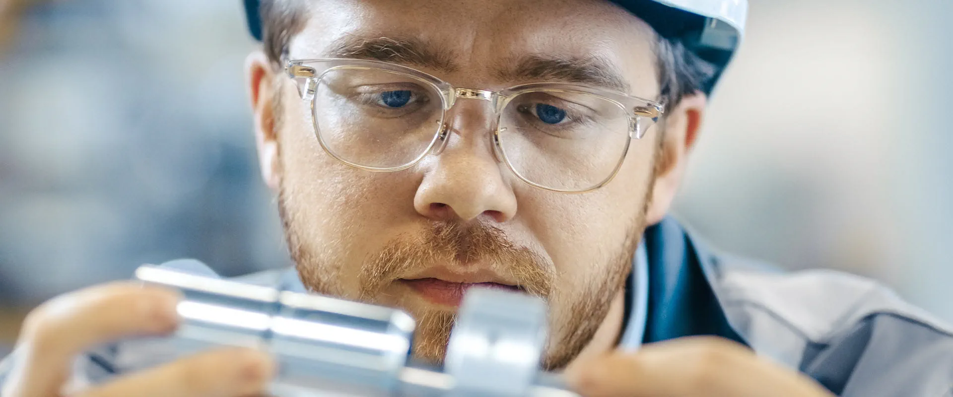 A focused engineer wearing safety glasses and a hard hat, inspecting a metal component.
