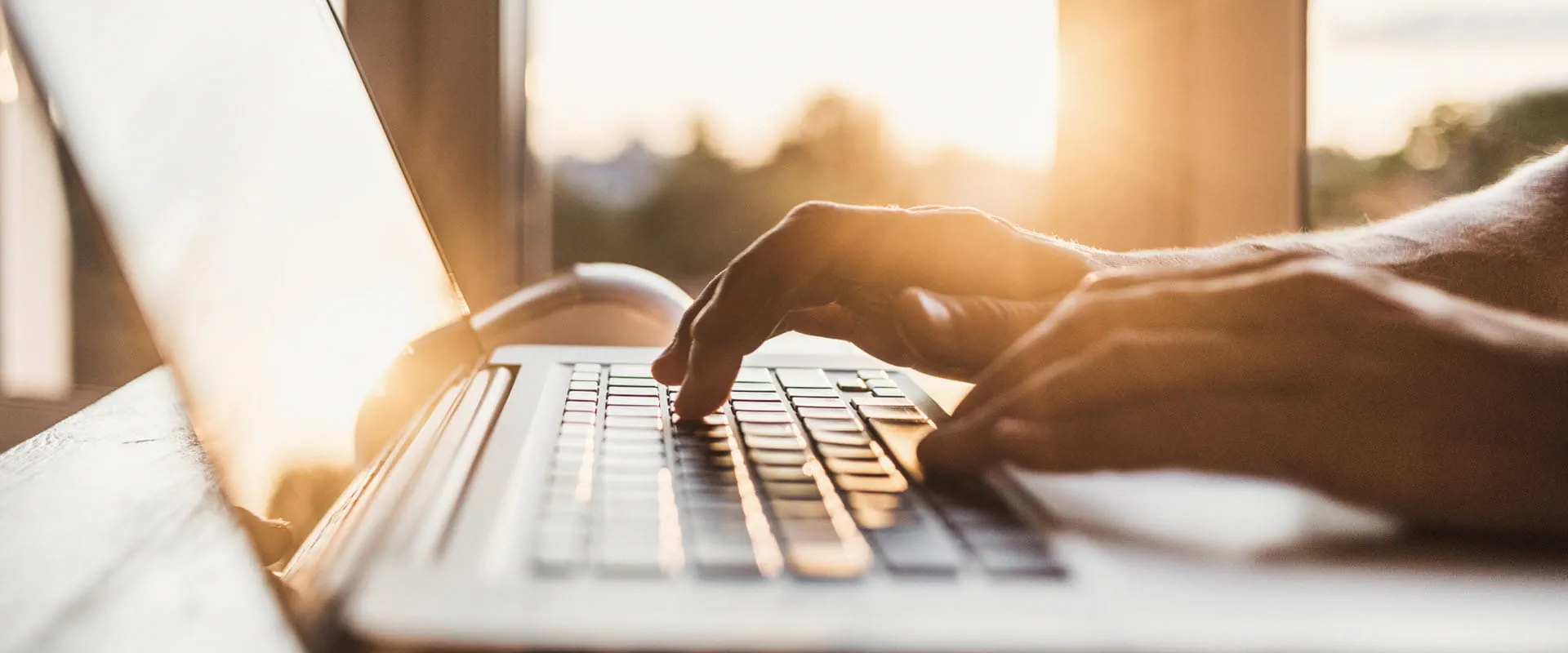 Close-up of hands typing on a laptop keyboard with sunlight streaming through a window.