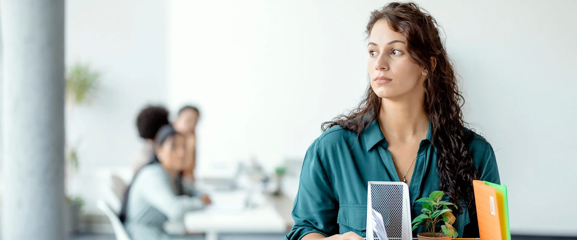 A professional carrying personal belongings, including a plant and folders, while leaving the office.