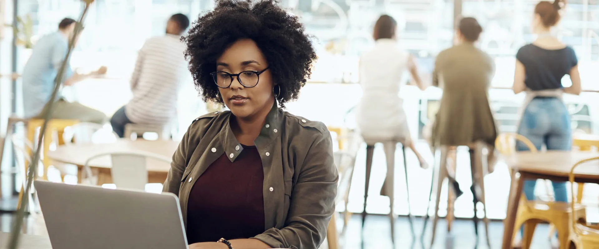 A person sits in a busy coffee shopping, looking at their laptop.