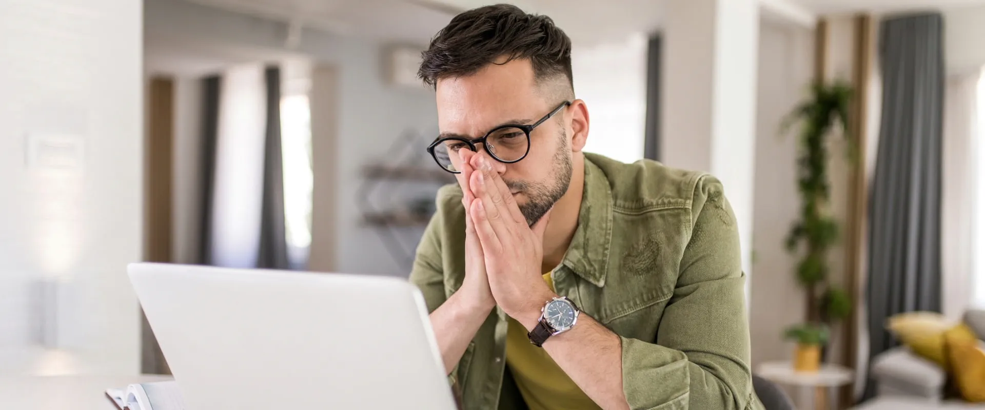 A person at home looks at their computer screen, seeming stressed.