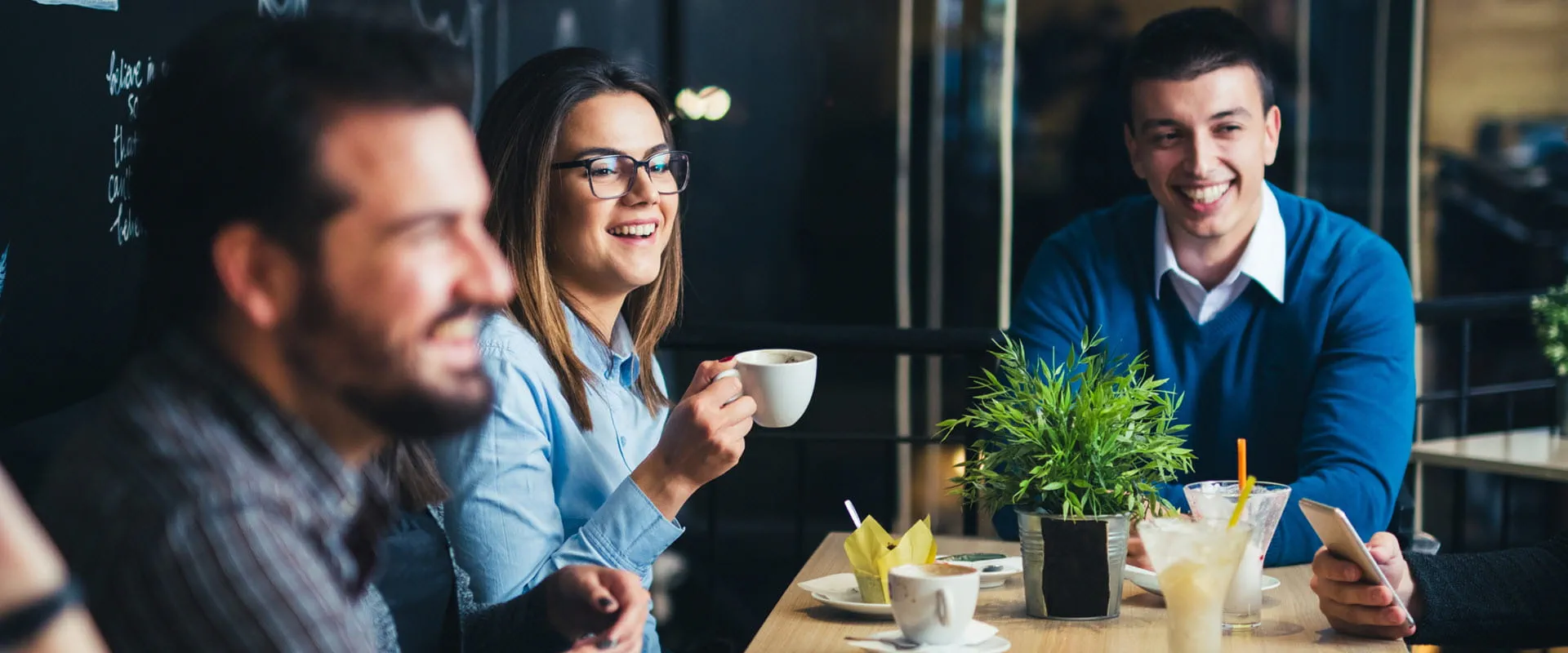 A group of young people sit around a table drinking coffee at a restaurant.