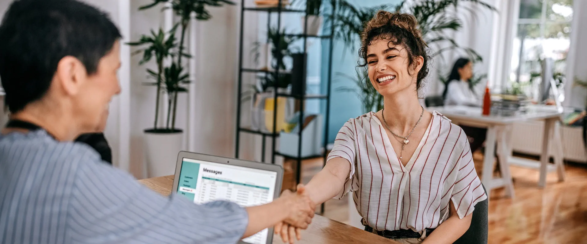 A smiling woman shaking hands with a recruiter during a job interview in a modern office setting.