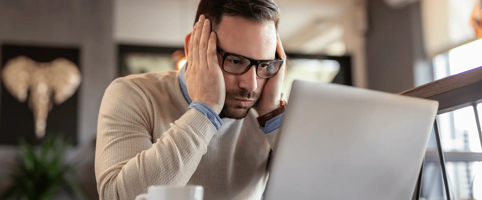 A person looks at their laptop in a coffee shop, seemingly frustrated.
