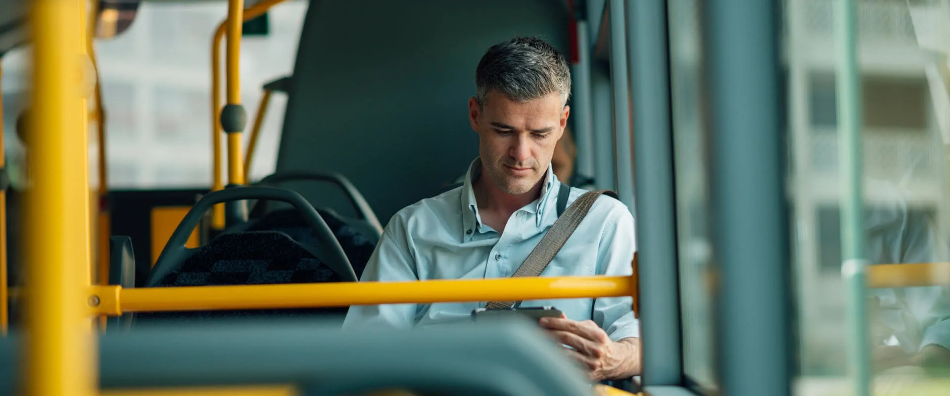 A person sitting alone on a bus, looking at their smartphone with a focused expression.