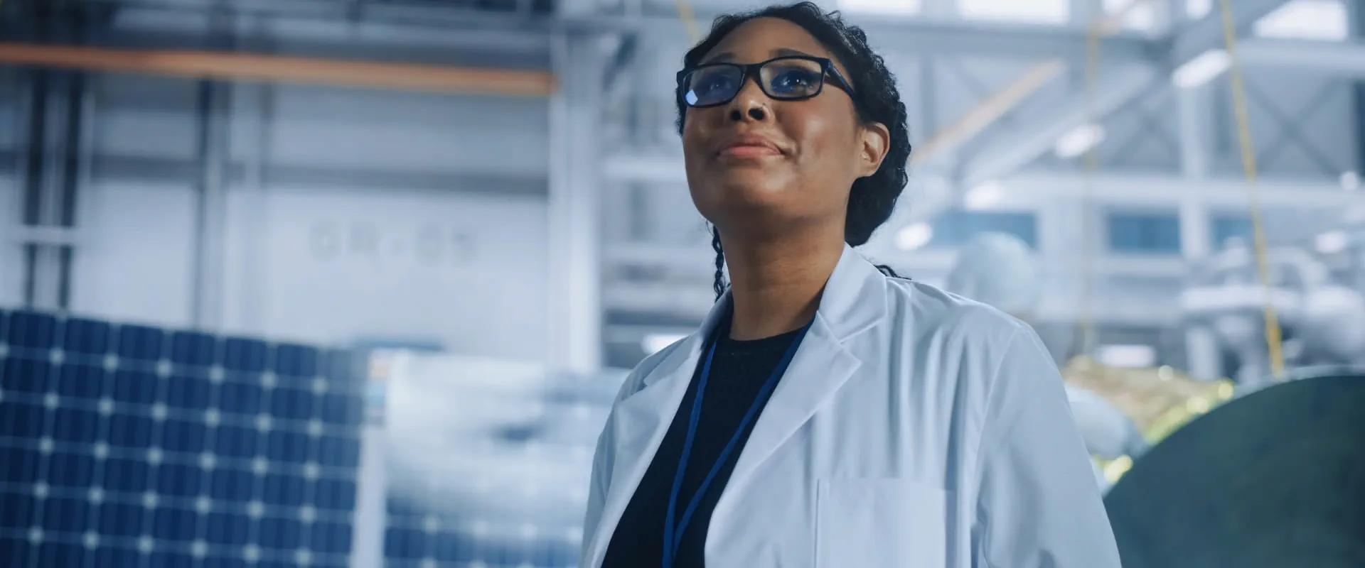 A worker looks upward, standing in a warehouse with solar panels behind them.