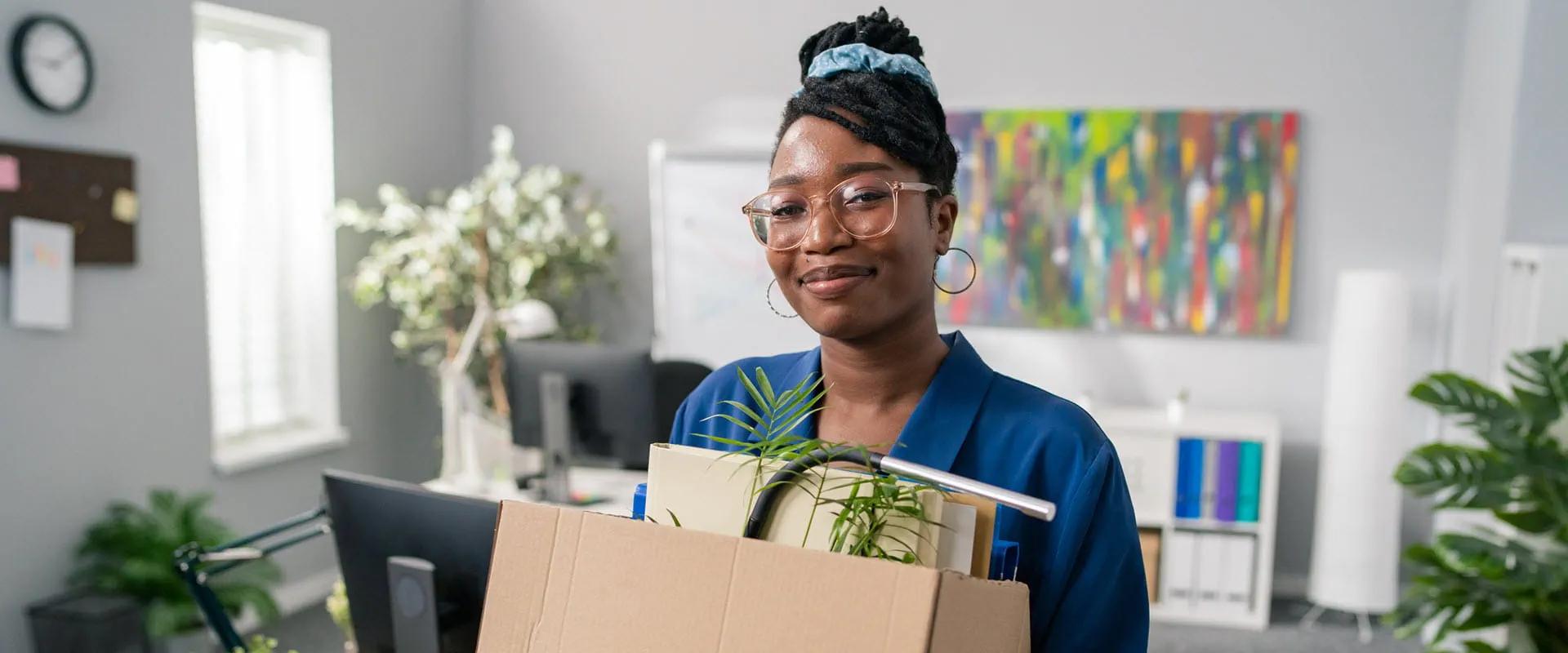 After quitting, a smiling individual walks out of an office with a box of files and plant