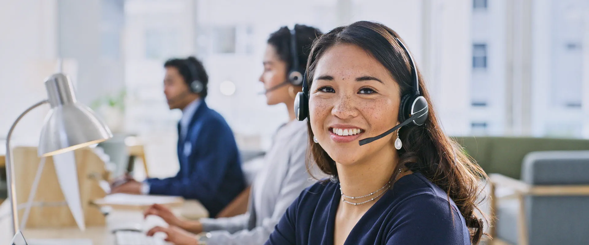 Customer service representatives wearing headsets, working in a modern office setting.