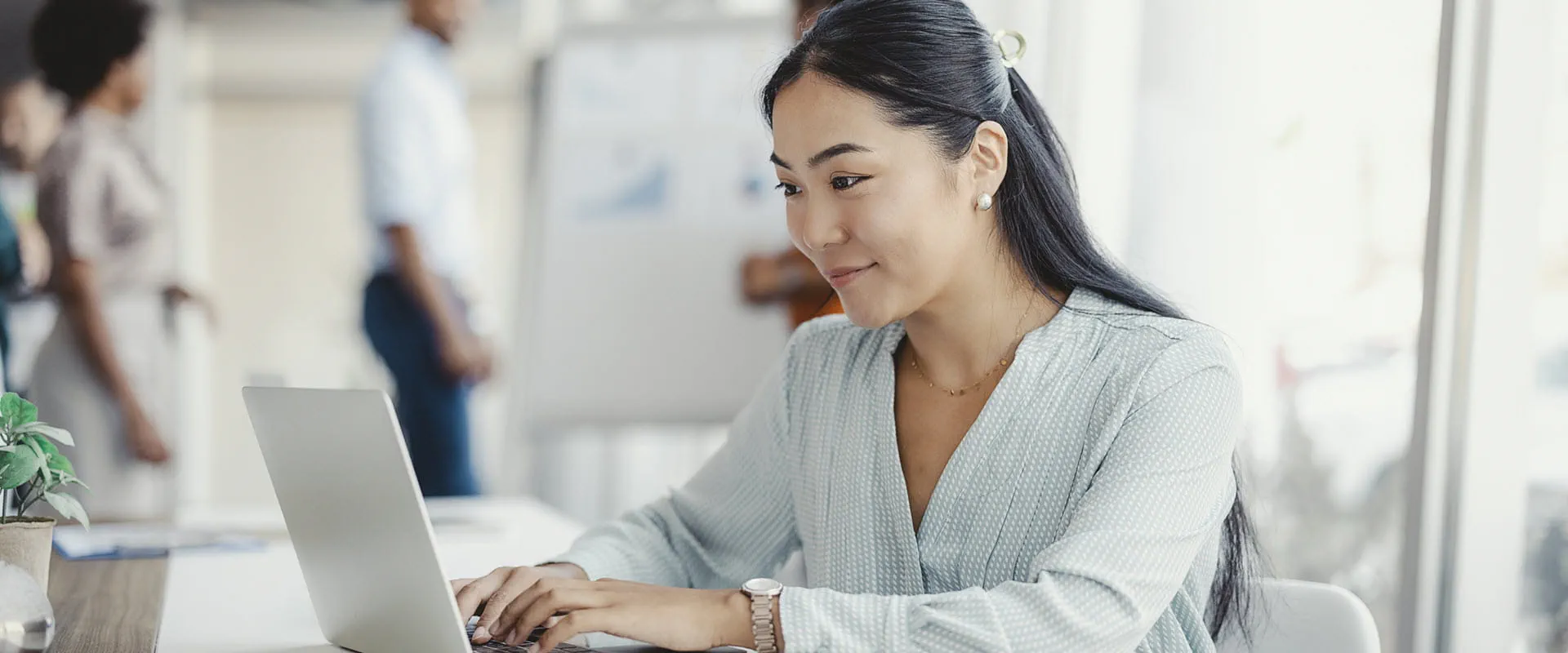 An individual in an office sits at a desk, typing at a laptop.