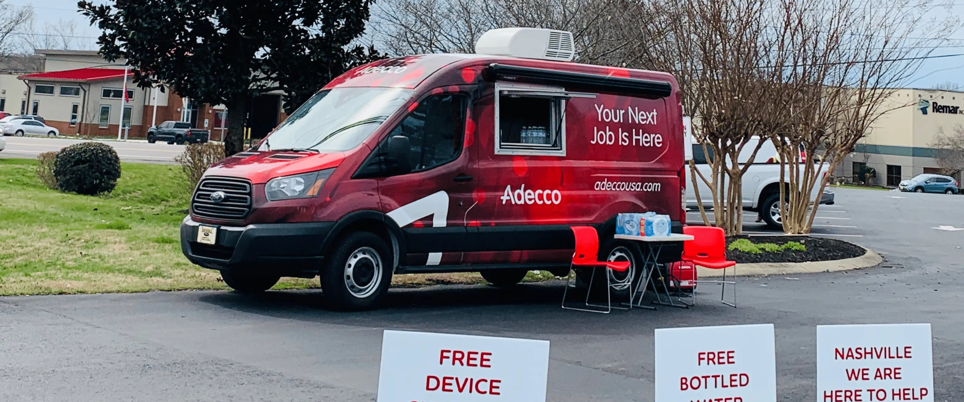 A red van with Adecco logos sits in a driveway. There are chairs sitting out front and a small table.