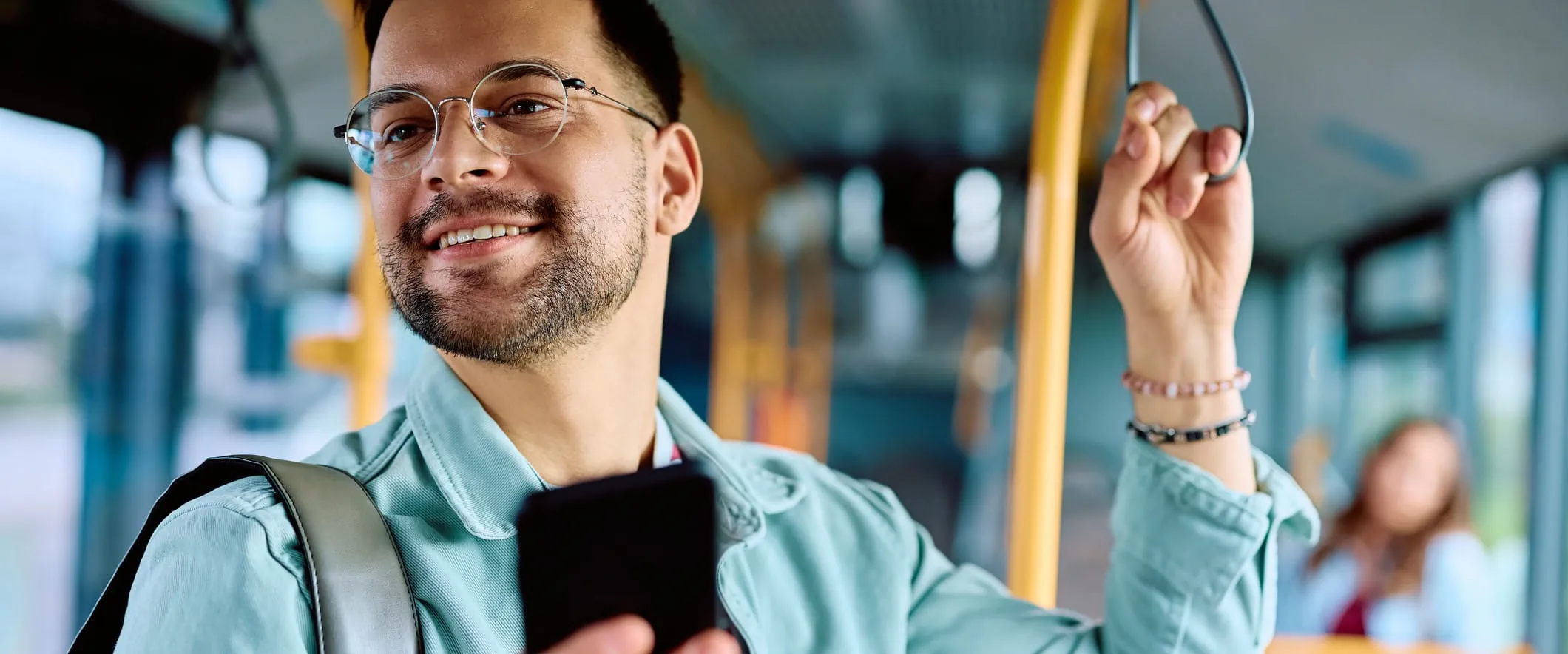 A person stands on a bus holding the support pole and their phone in the other hand