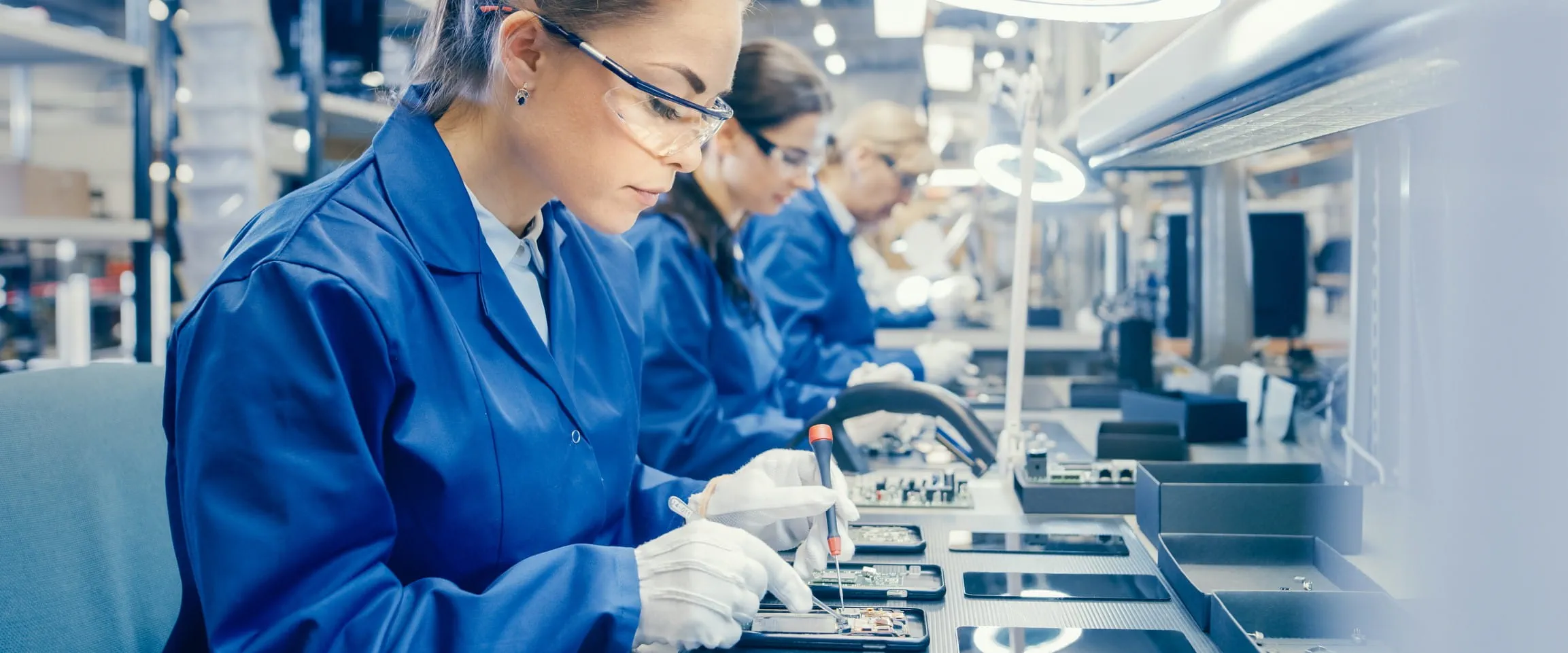 A line of workers in a clean facility, work on what appears to be cell phones