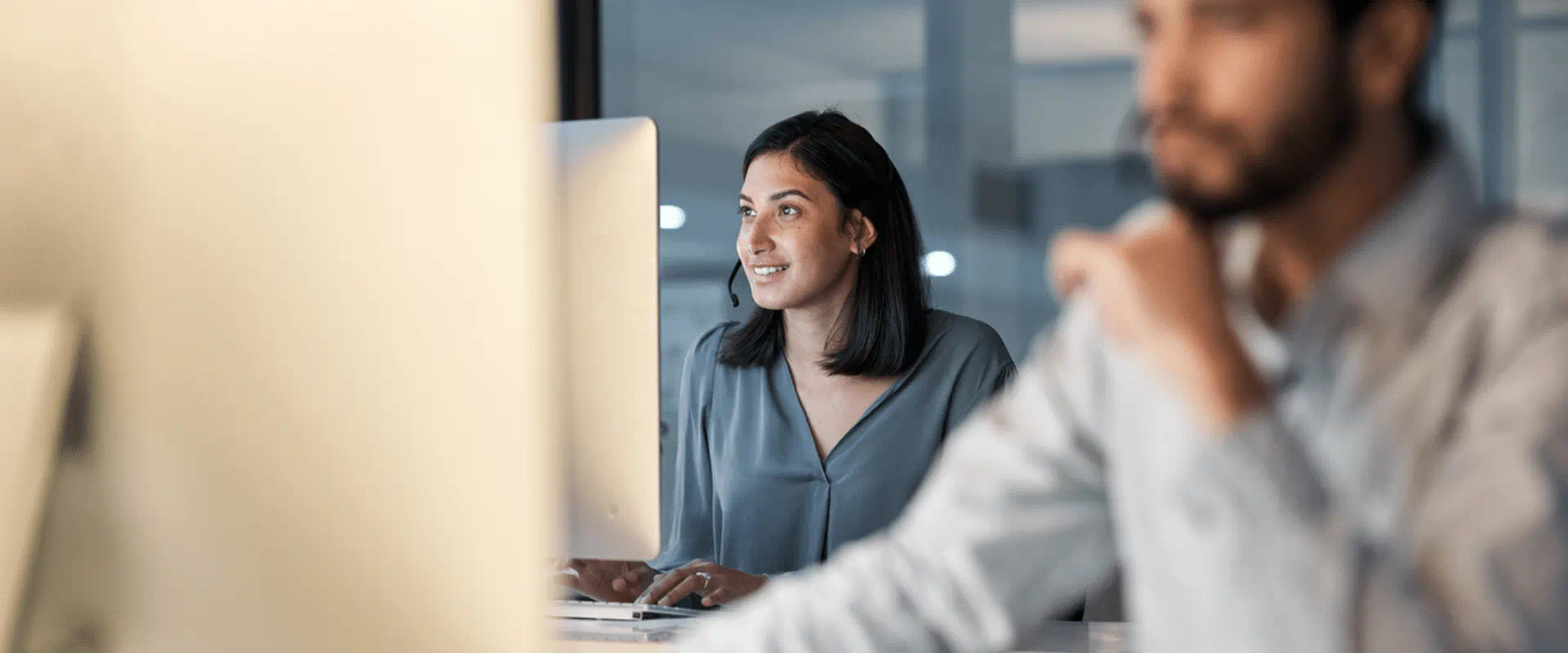 A call center worker smiles while looking at their computer, in a busy office