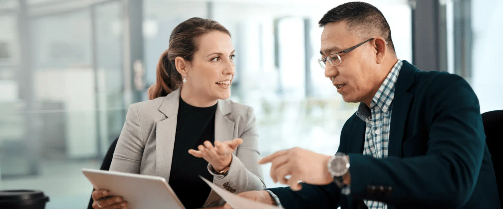 Two people sit at a desk, looking over papers