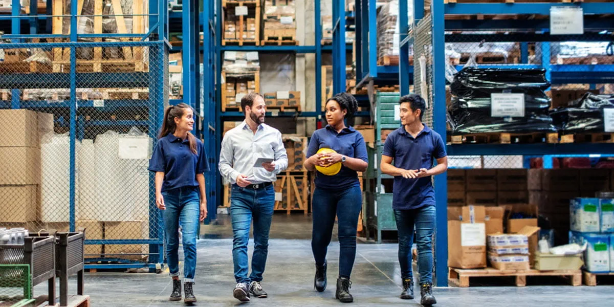 Group of warehouse employees walking by storage racks.