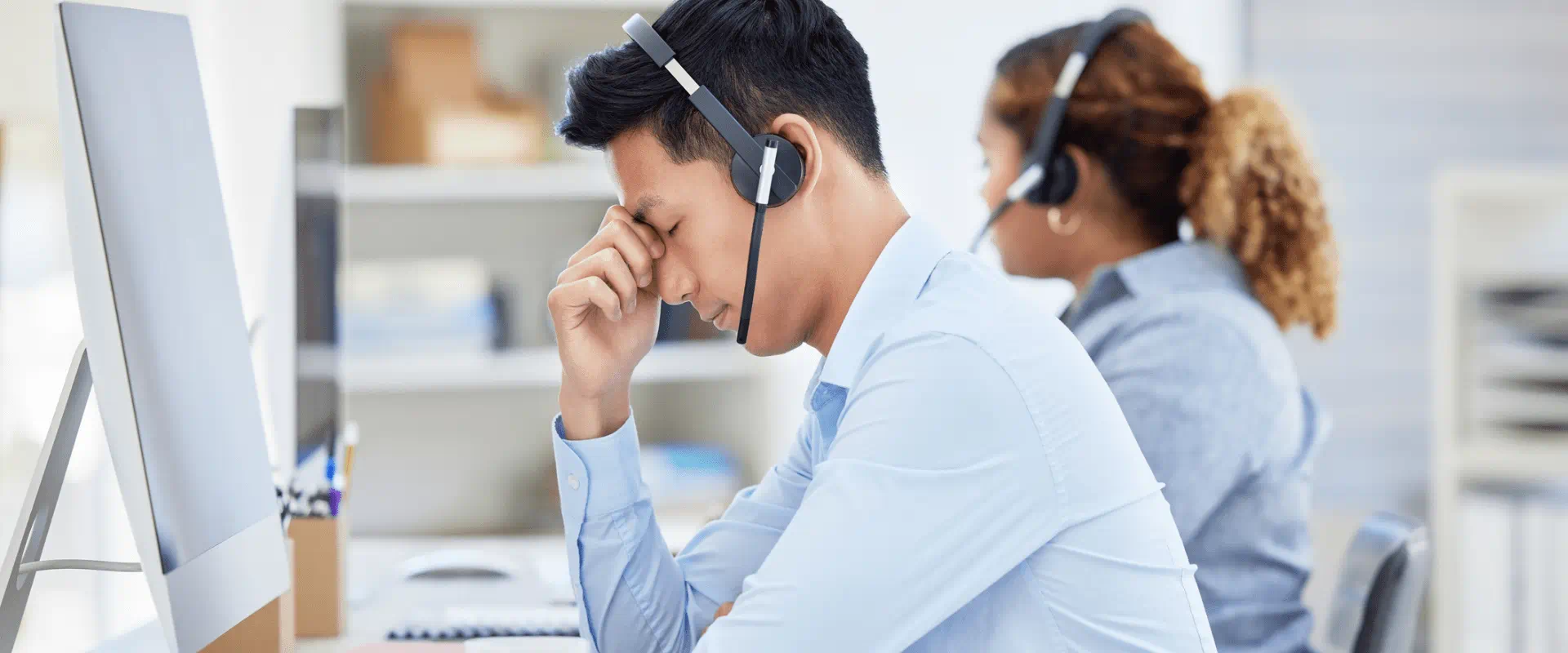 A call center worker sits in an office, they look tired and irritated. 