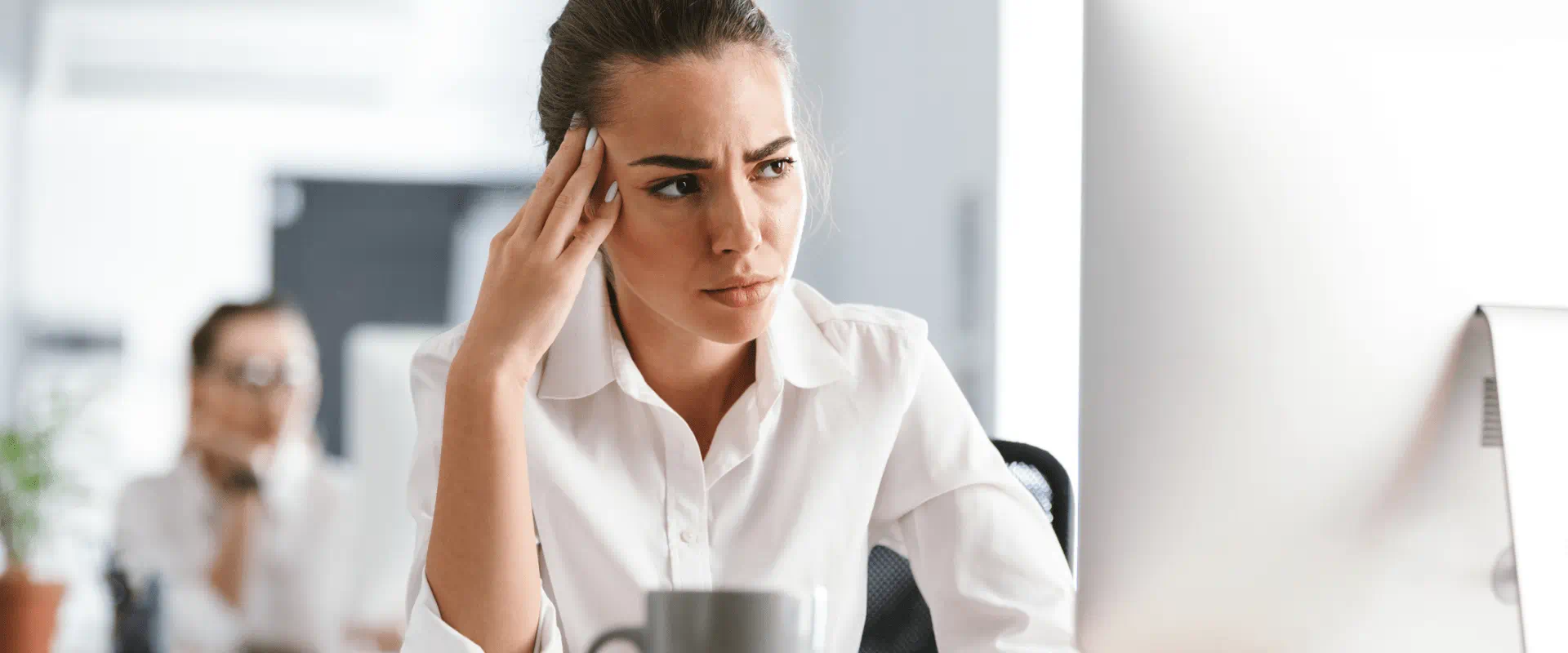 A frustrated worker looks at their desktop computer in an open office.