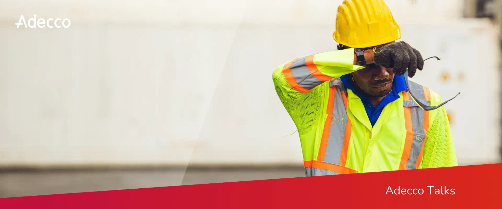 A worker wearing a safety vest and hard hat wipes sweat from their forehead.