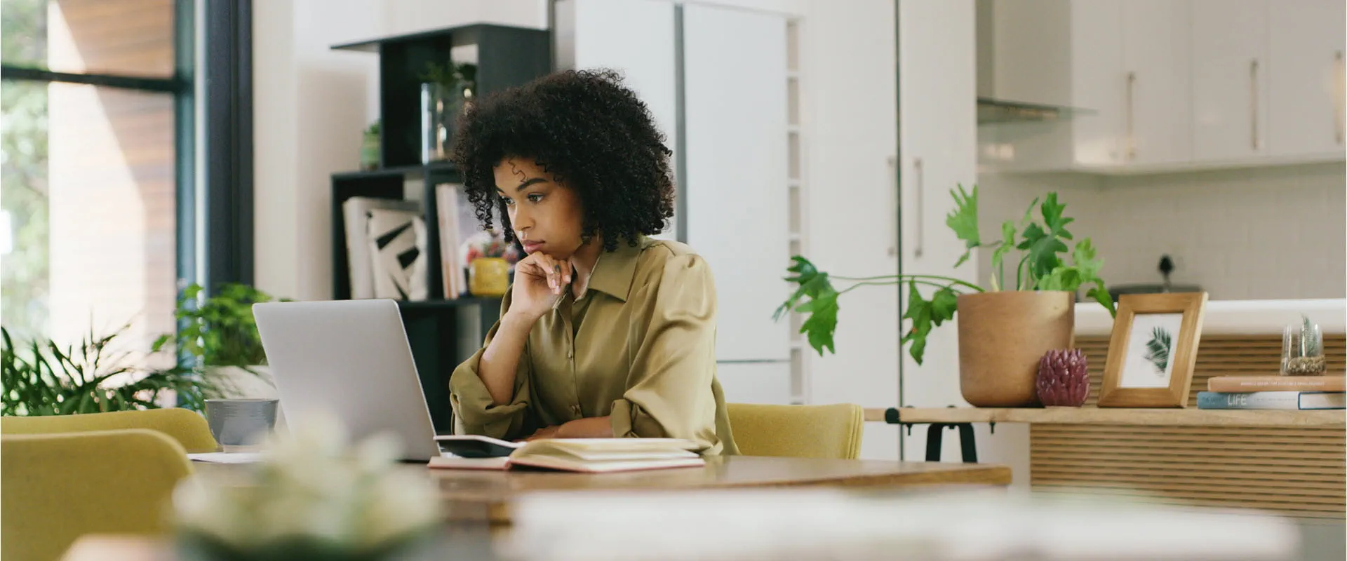 A woman sits at home looking pensively at her laptop.