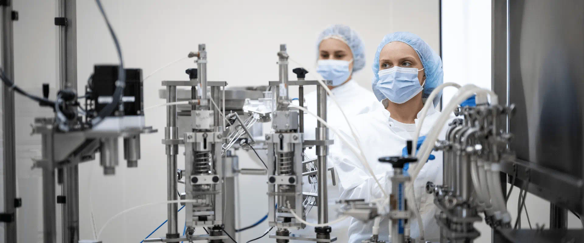 Two people in protective gear work at a biomanufacturing plant. 