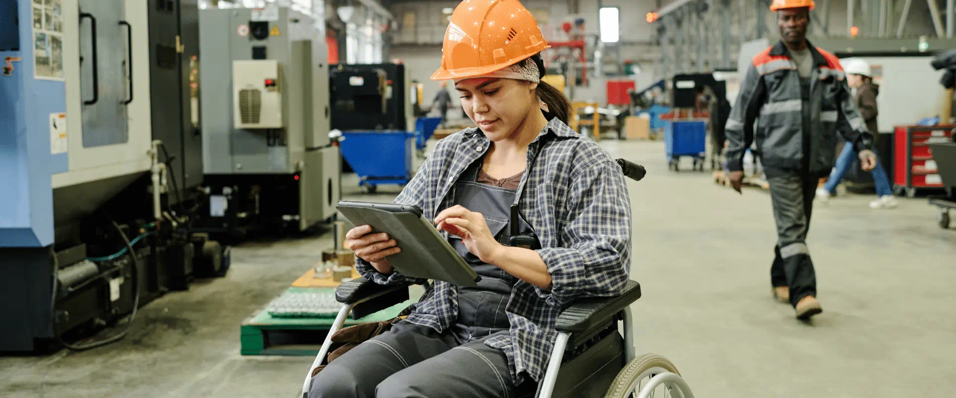 A worker in a wheelchair looks at a tablet on a manufacturing floor.