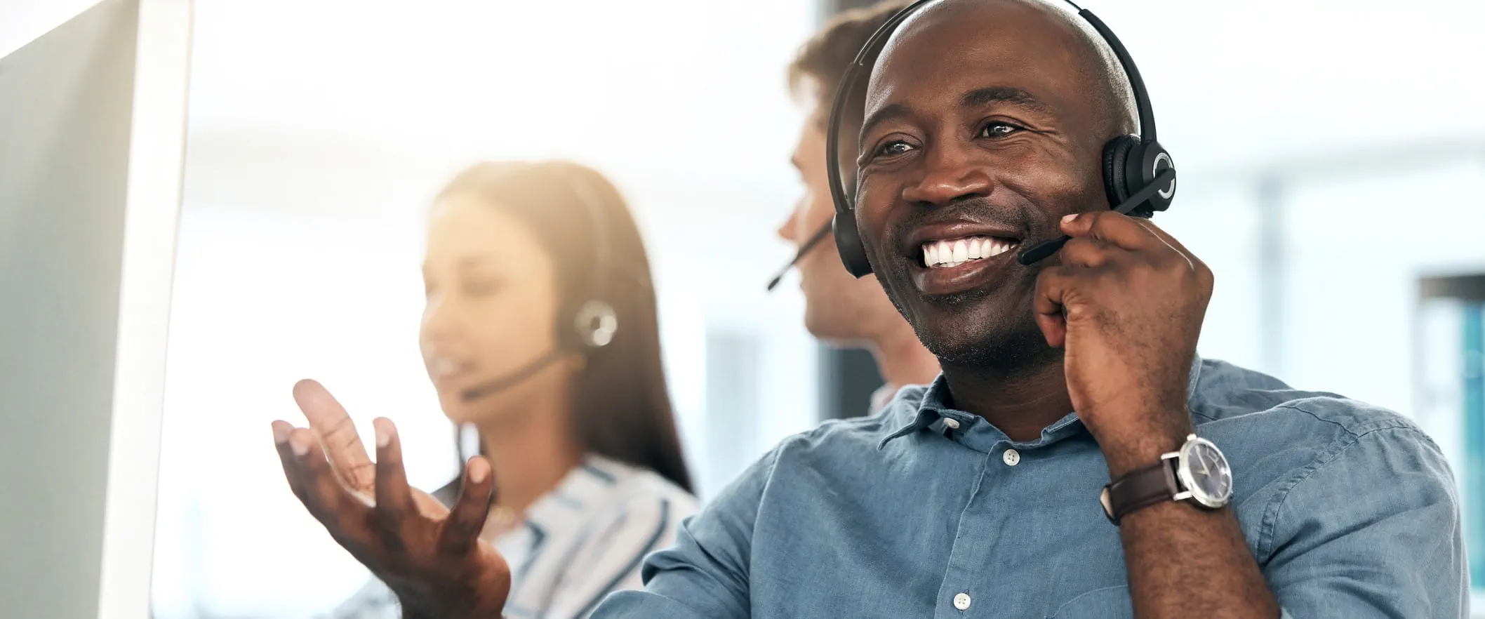 A call center smiles and talks, while wearing a headset. Other call center workers are behind them.