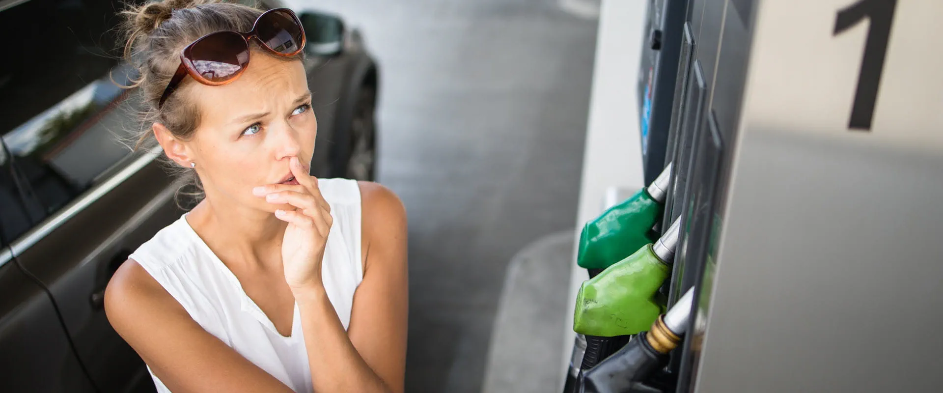 A person at a gas station has their hand on the pump, but they're looking at the prices concerned