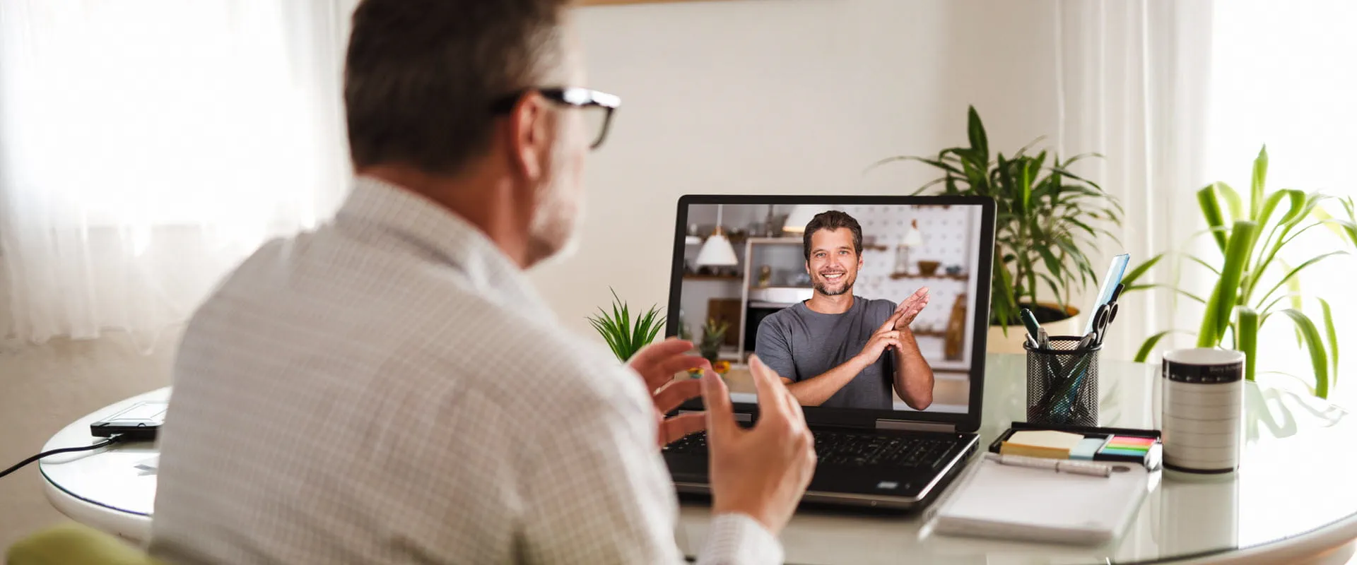 An individual with glasses signs with another person, via video chat, on their laptop.