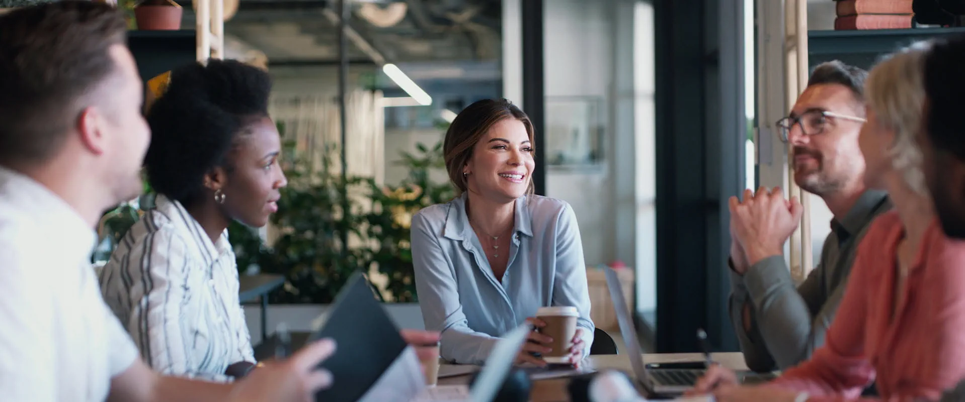 A group of workers in casual business attire sit around a conference table smiling