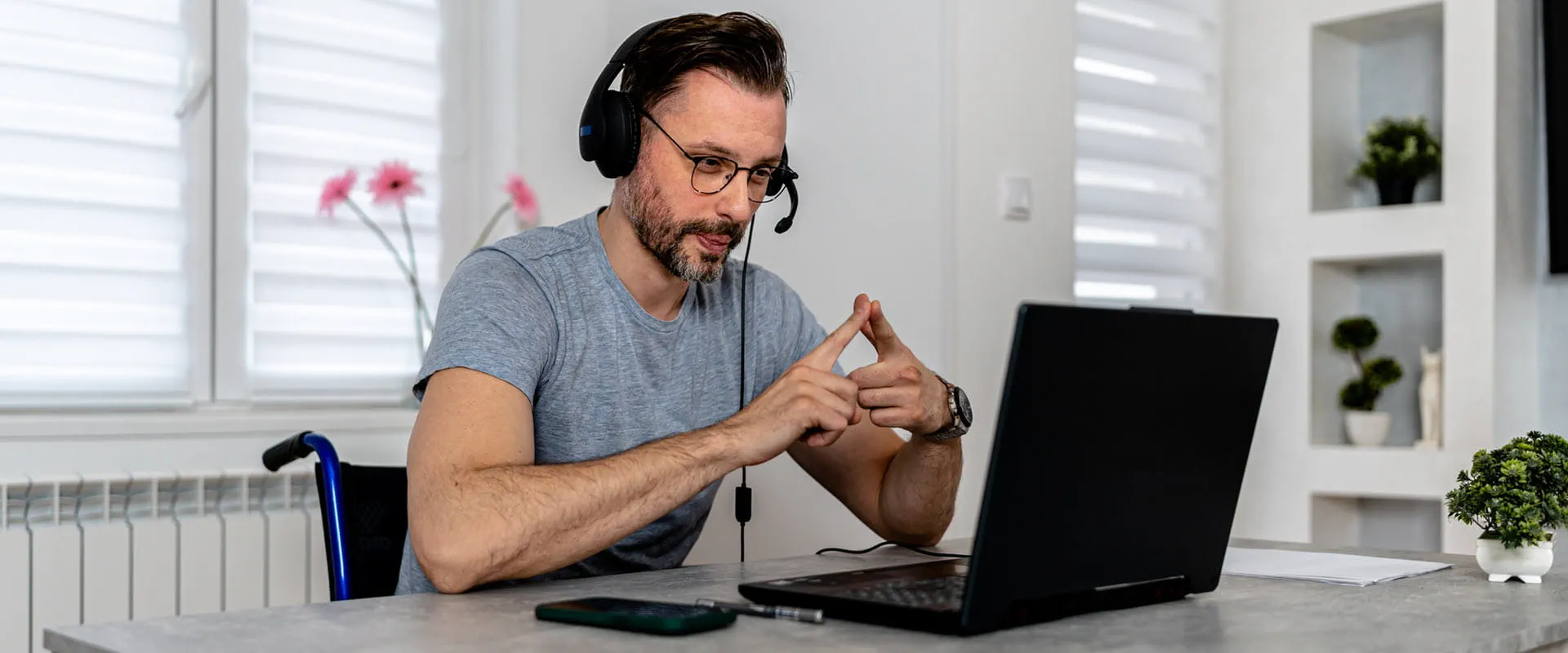 A person sitting in a wheelchair wearing a headset on a video call on laptop.