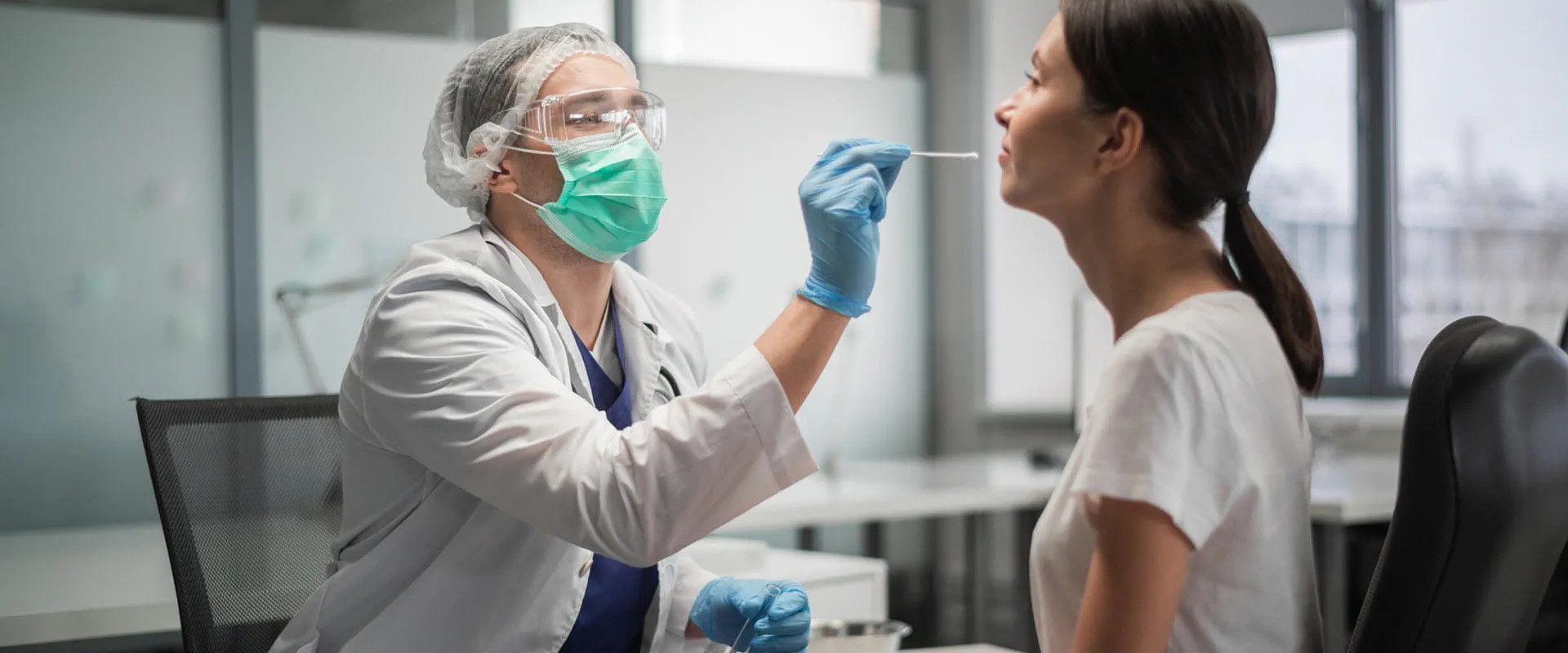 Masked and gloved individual taking a swab from a patient.