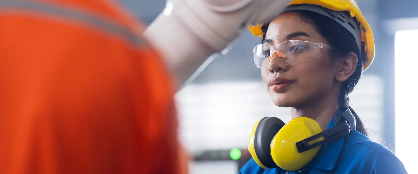A worker listens and concentrates, while wearing a hard hate, safety glasses, and safety ear muffs around their neck