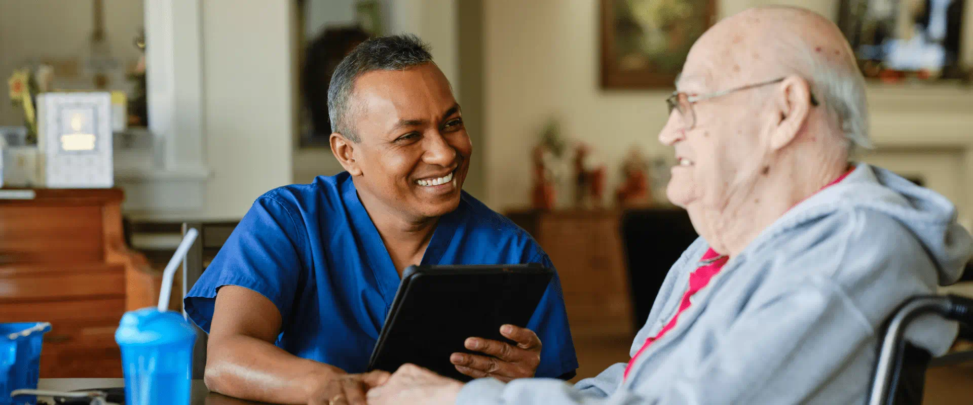 A nurse sits at a table with a person in a wheelchair at a care facility. 