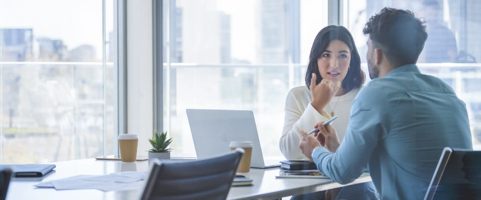 Two professionals having a focused discussion in a modern office with large windows and a city skyline in the background. Two professionals having a focused discussion in a modern office with large windows and a city skyline in the background.
