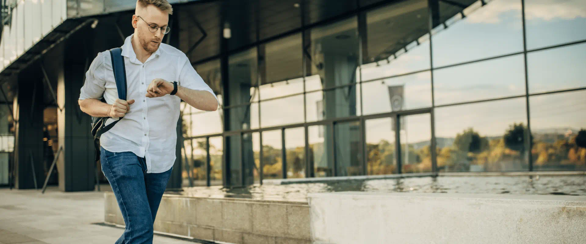 A person in jeans and a button-up shirt jogs outside a building, while looking at their watch