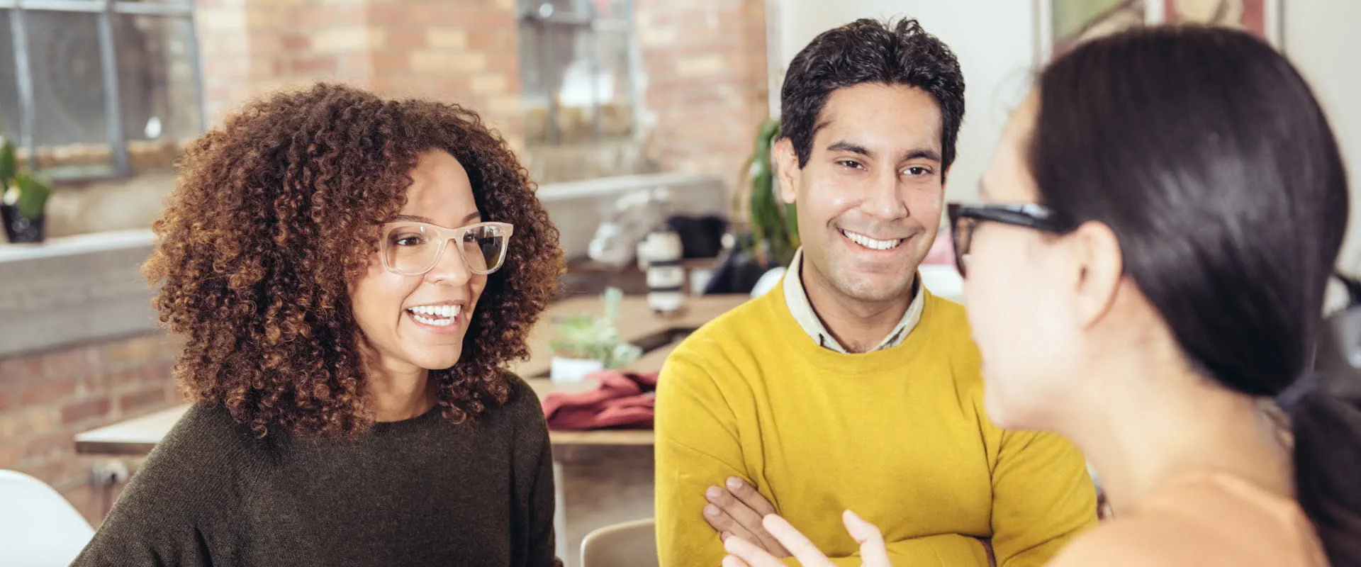 Three professionals engaged in a friendly conversation in a modern office or coworking space.